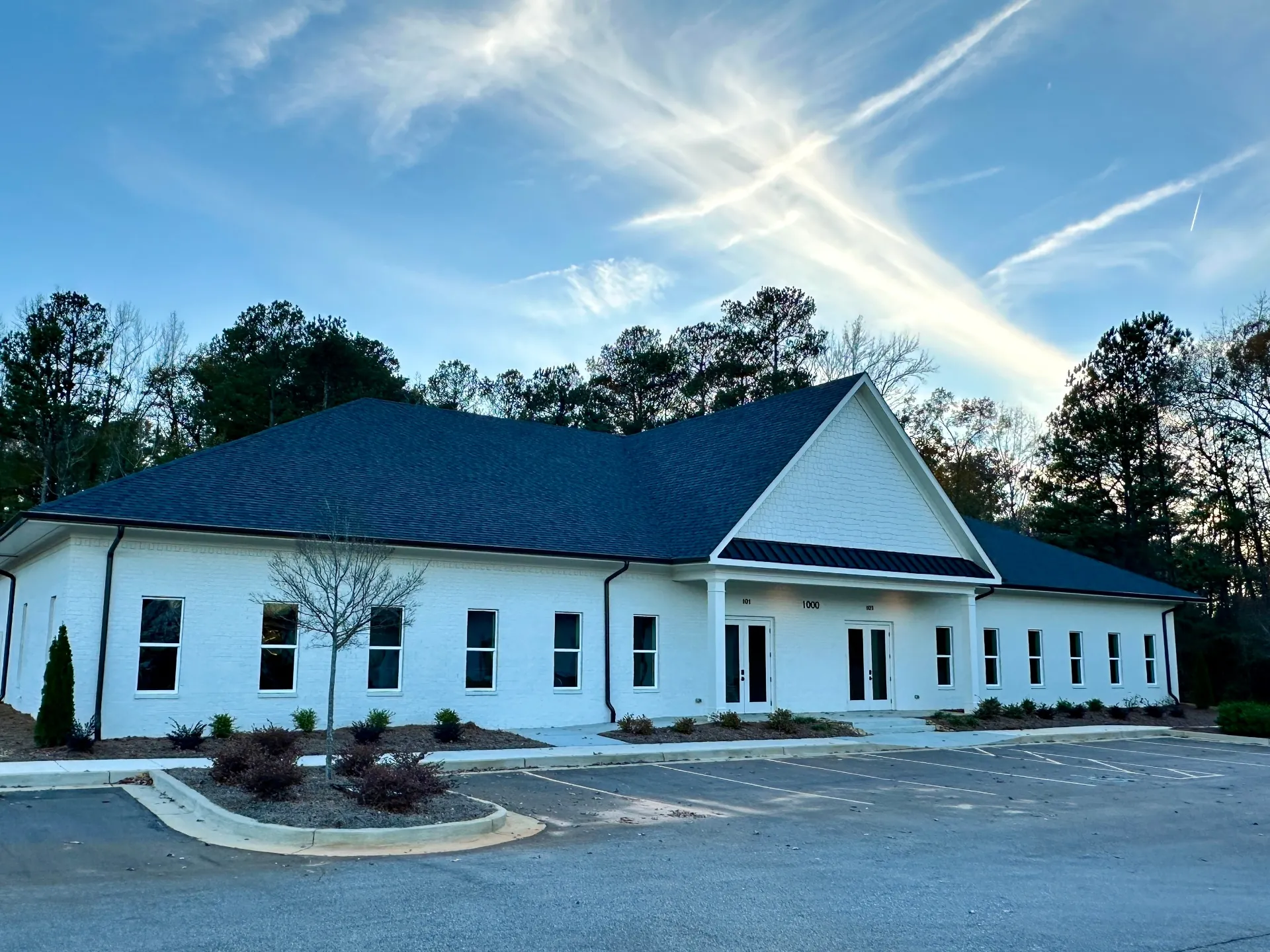 White-painted brick professional office building with gabled entry portico and landscaped parking